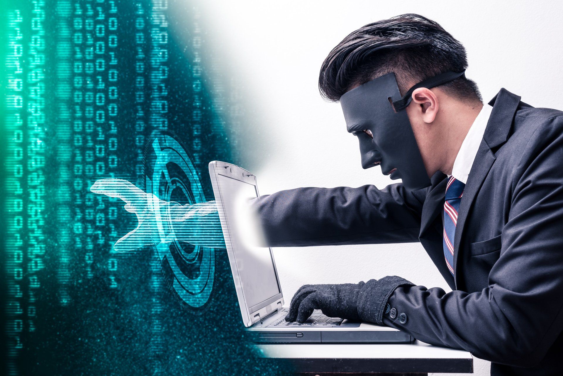 Cybercriminal in mask reaching toward laptop, symbolizing hacking and digital security breach attempt.