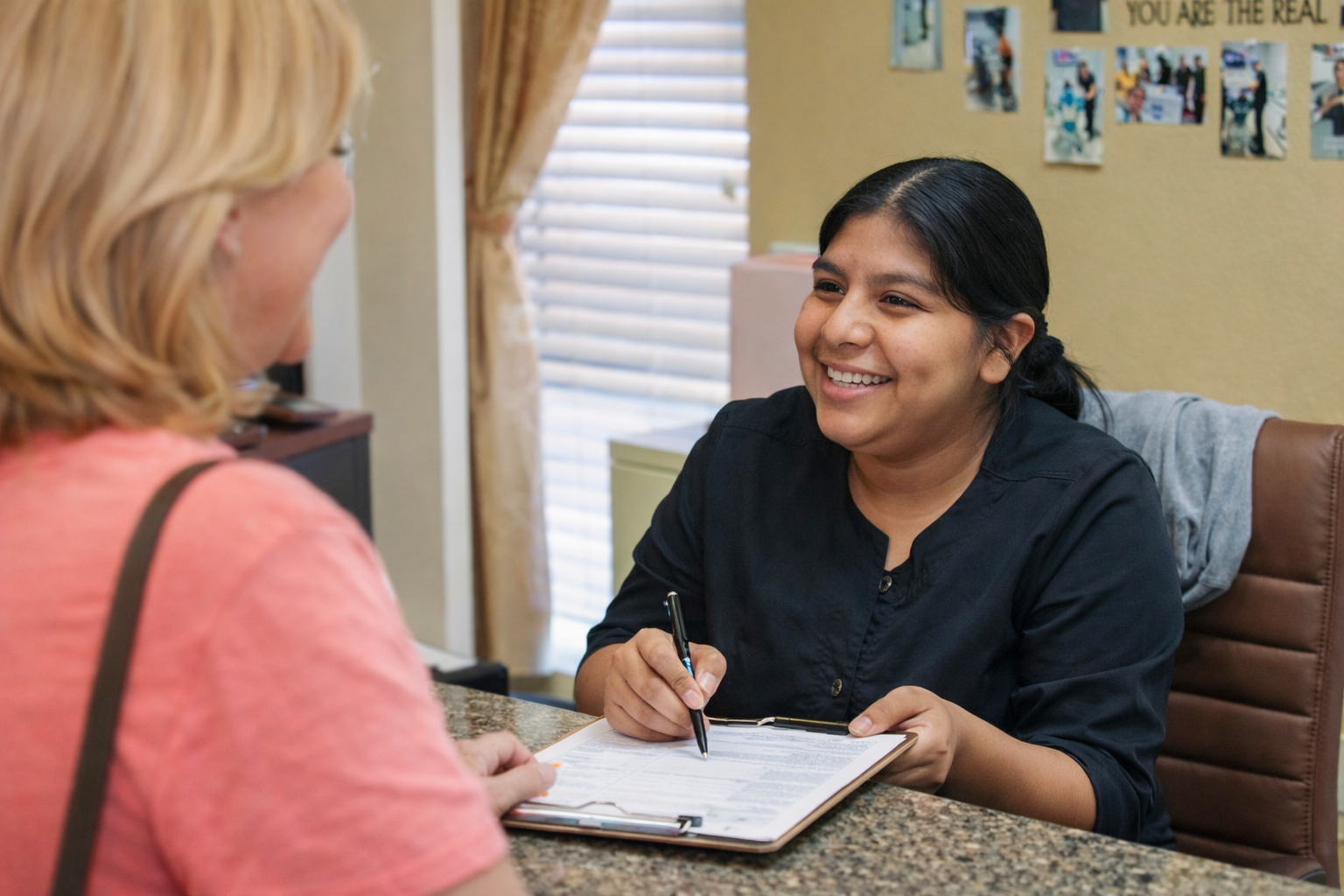 Smiling woman takes notes across a desk during a consultation in an office