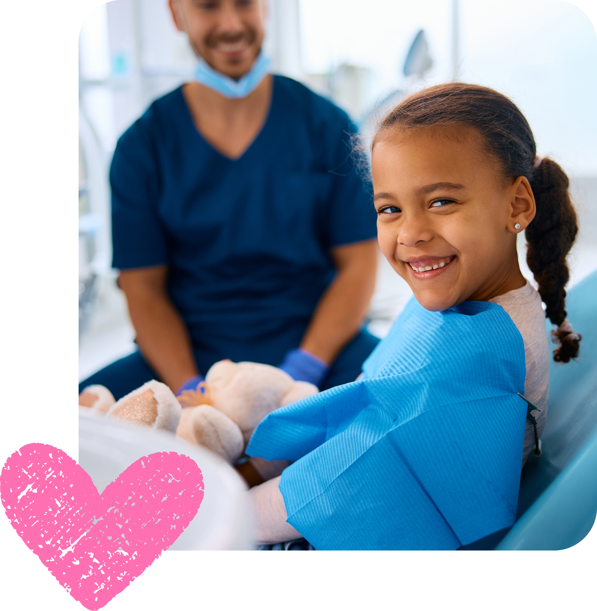 A smiling child sits in a dental chair with a toy, while a dentist in blue scrubs and a mask sits in the background.