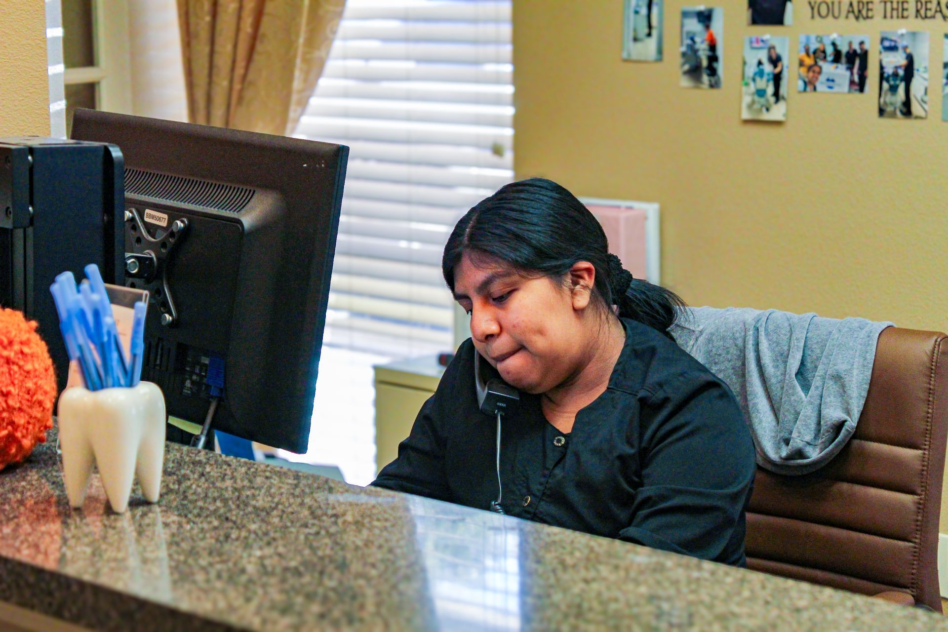 Person seated at an office desk with a computer monitor, writing in a notebook, in a beige office.