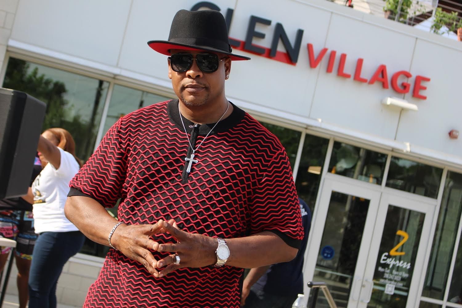 A man wearing a hat and sunglasses is standing in front of a building that says glen village.