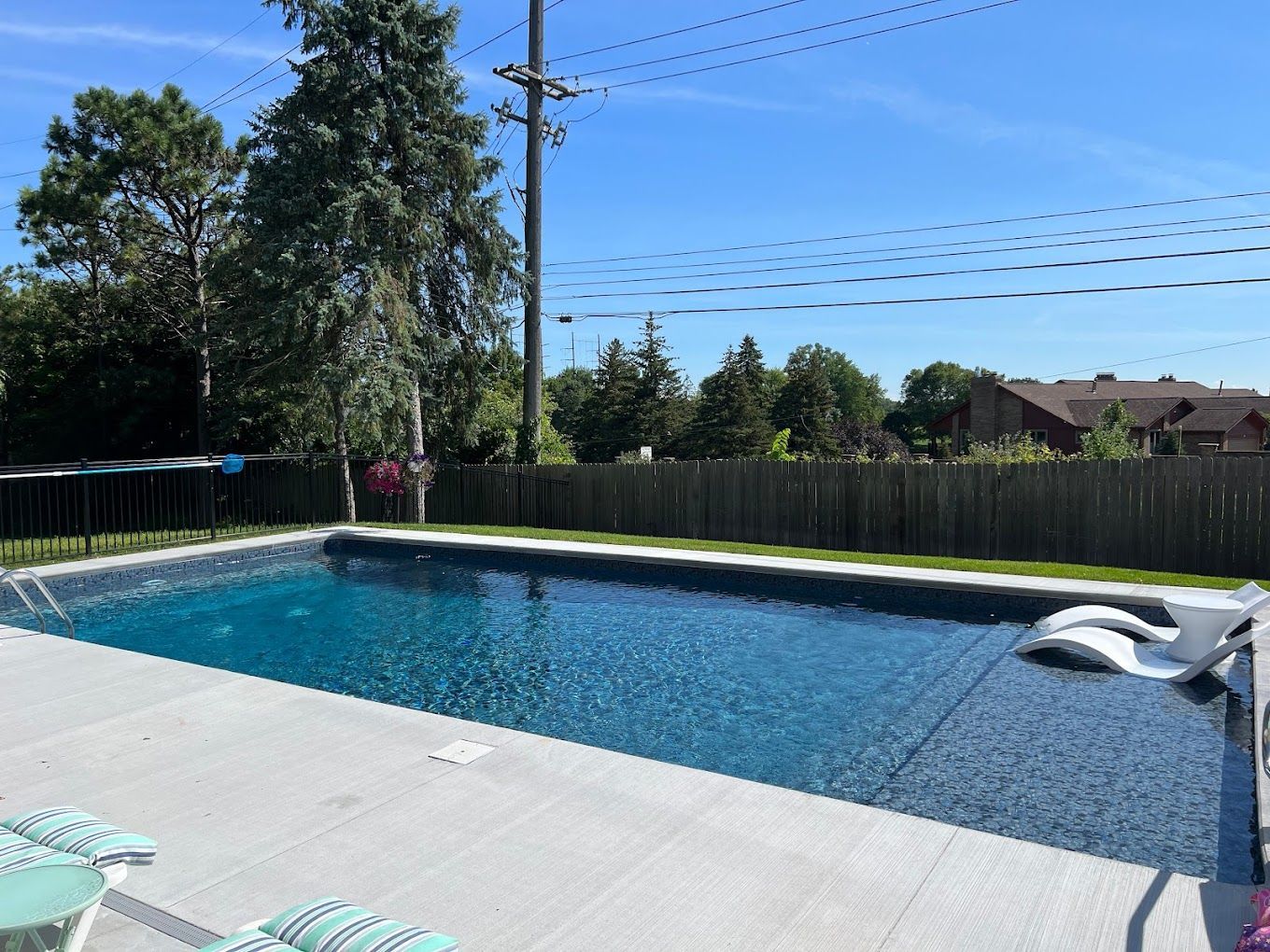 A large swimming pool in a backyard with chairs and a fence.