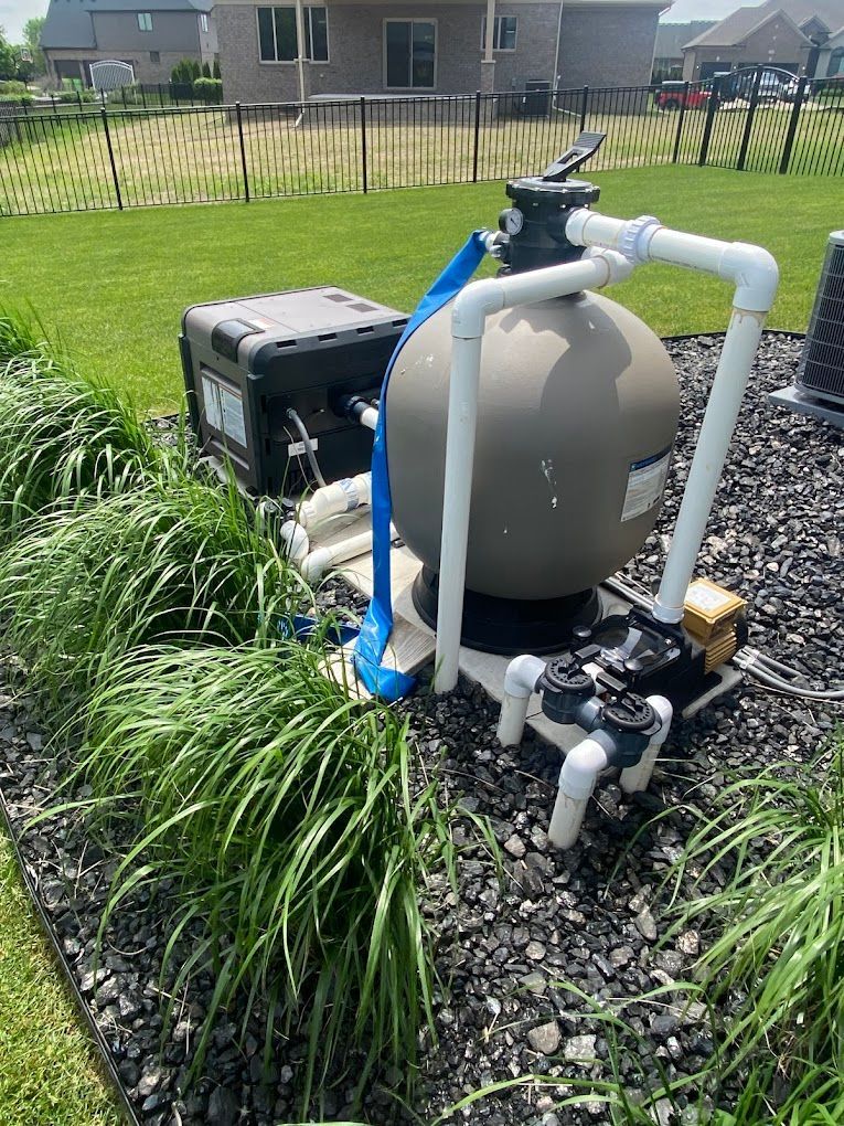 A sand filter is sitting on top of a pile of gravel next to a fence.
