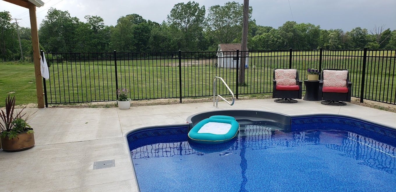 A large swimming pool surrounded by a fence and chairs.