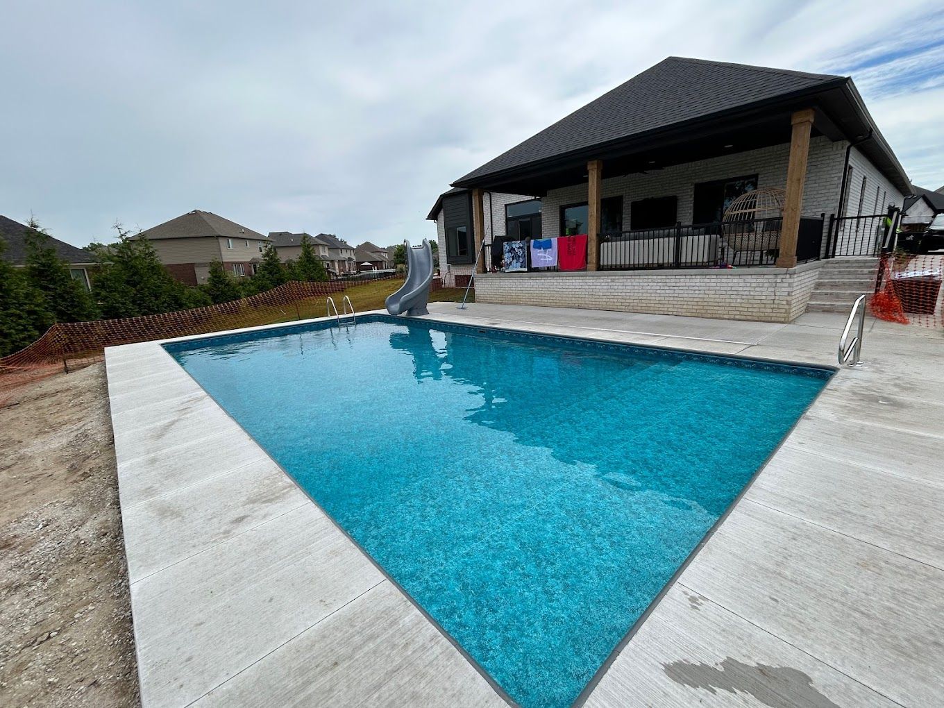 A large swimming pool with a slide in front of a house.