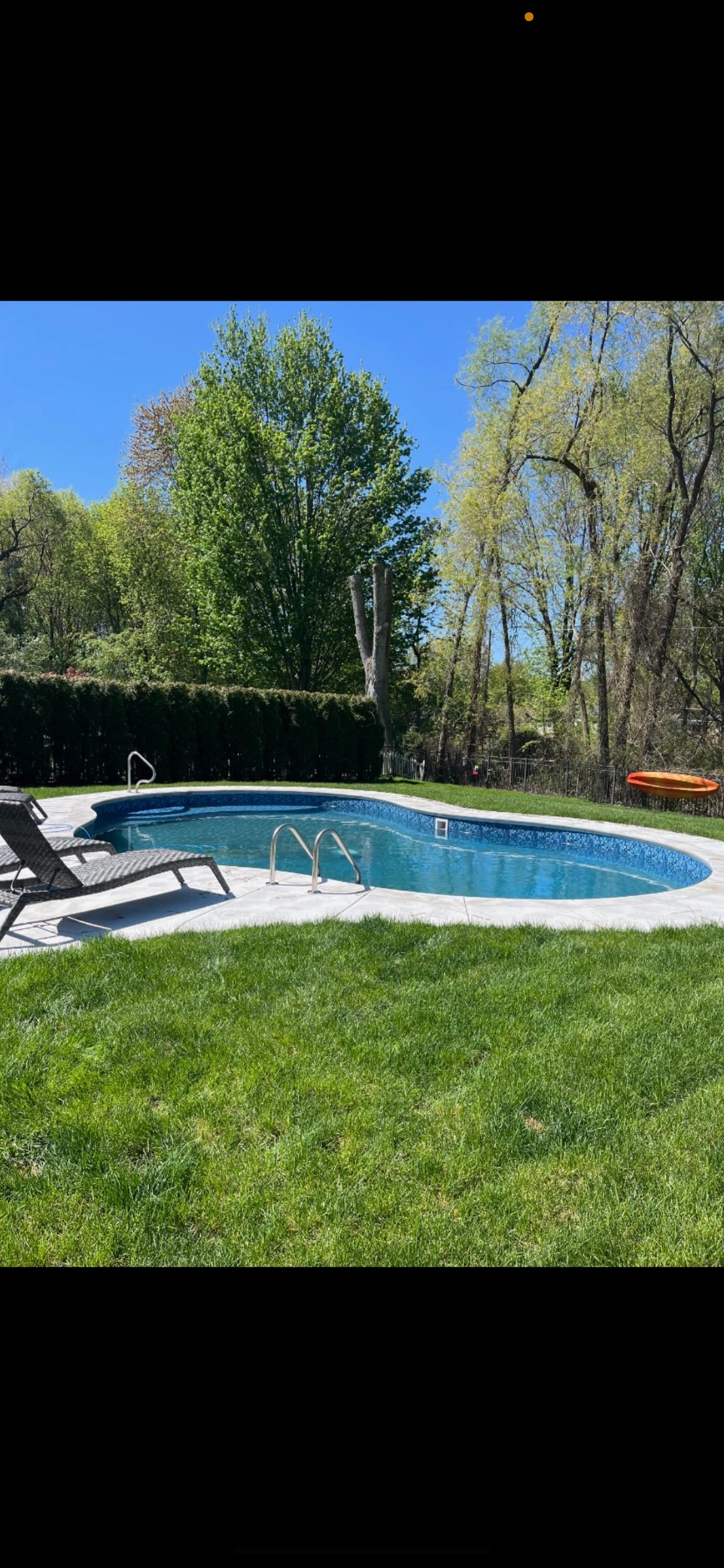 There is a large swimming pool in the middle of a lush green yard.