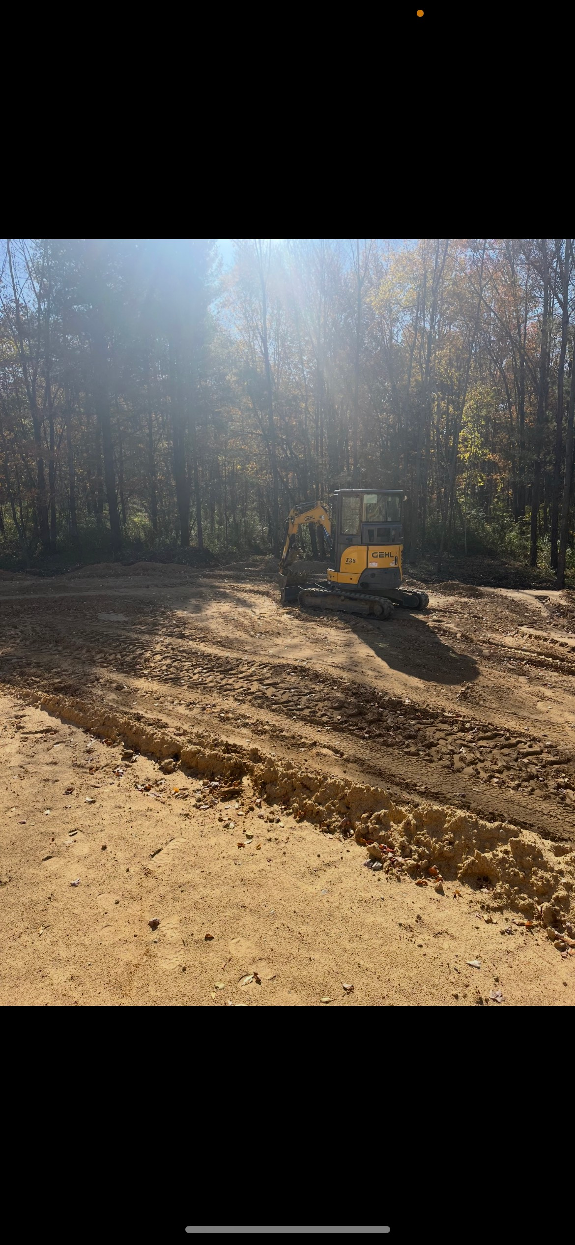A yellow excavator is working on a dirt road in the woods.