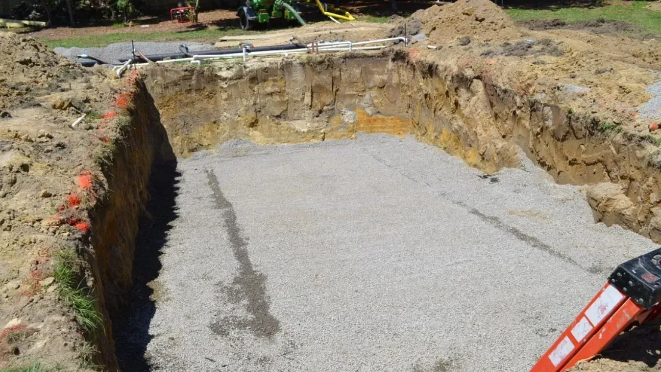 A rectangular hole excavated in the ground, filled with a layer of gray gravel for a construction project.