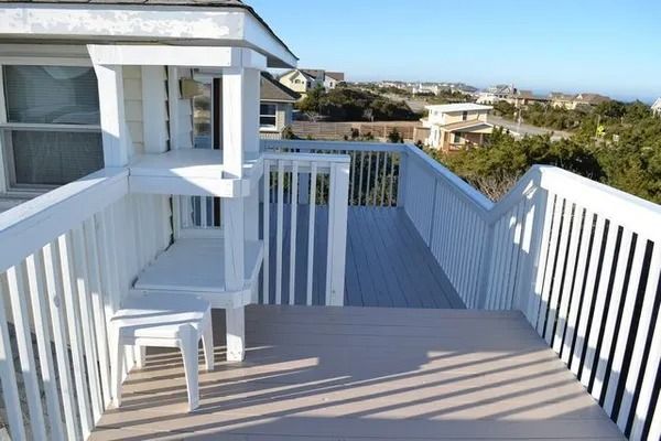 An elevated wooden deck with white railings, a multi-level built-in bench, and views of nearby coastal houses.