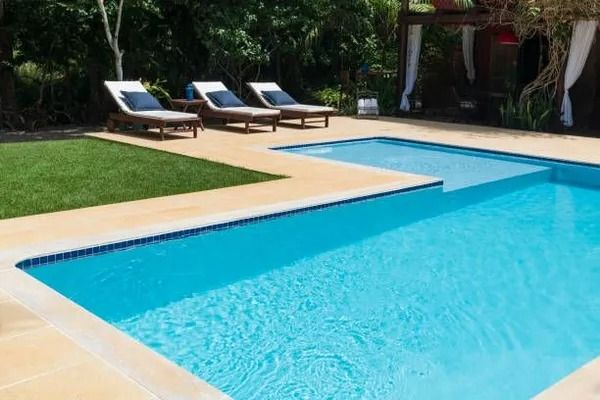 A swimming pool with clear blue water, adjacent to a green lawn and three lounge chairs on a light-colored patio deck.