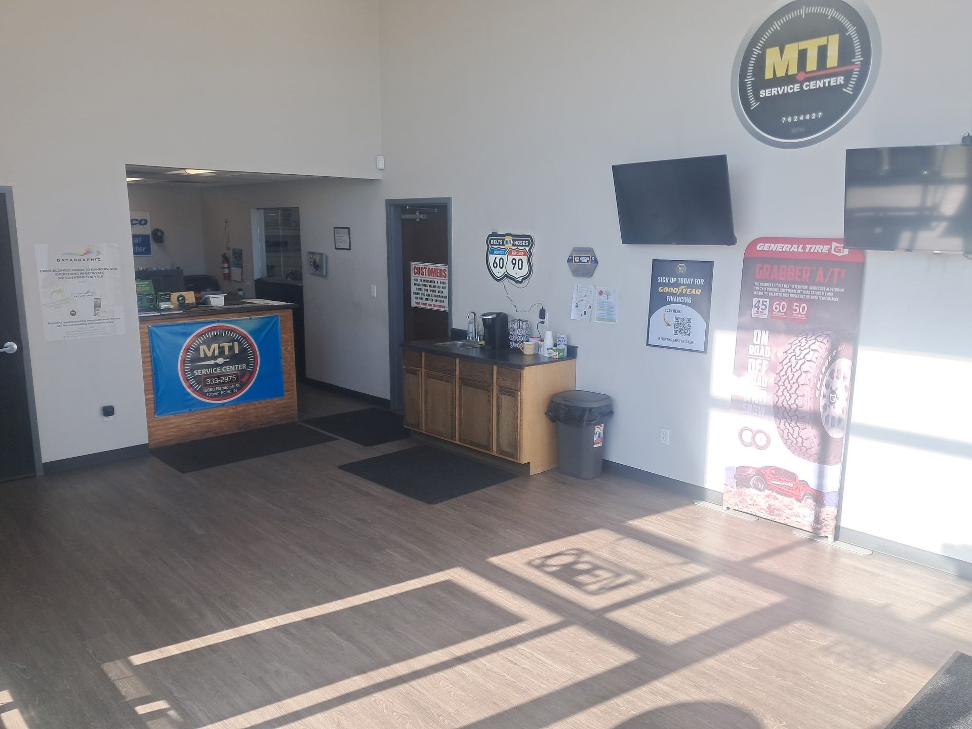 Empty lobby with MTI signs, a desk, TV, trash can, and bright sunlight on the floor.