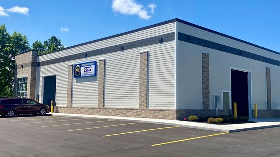 Exterior of a light gray commercial building with dark gray accents and a large door. Car parked out front.