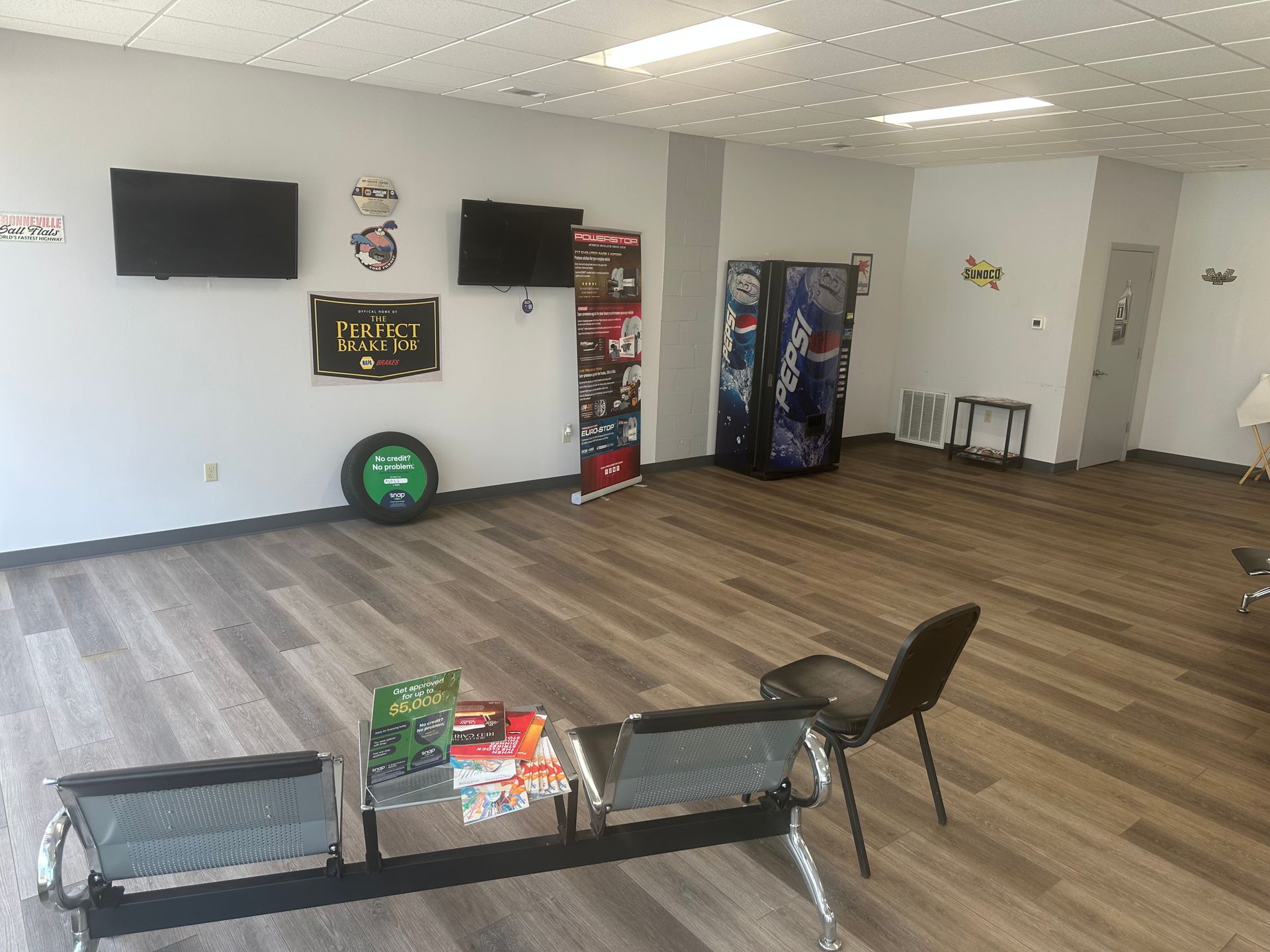 Empty indoor lounge with wall-mounted TVs, arcade machines, chairs, and wood-look flooring