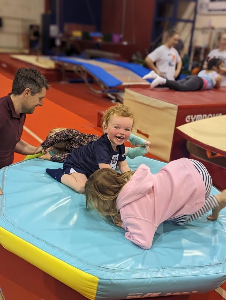 A man and two children are playing on a mat in a gym.