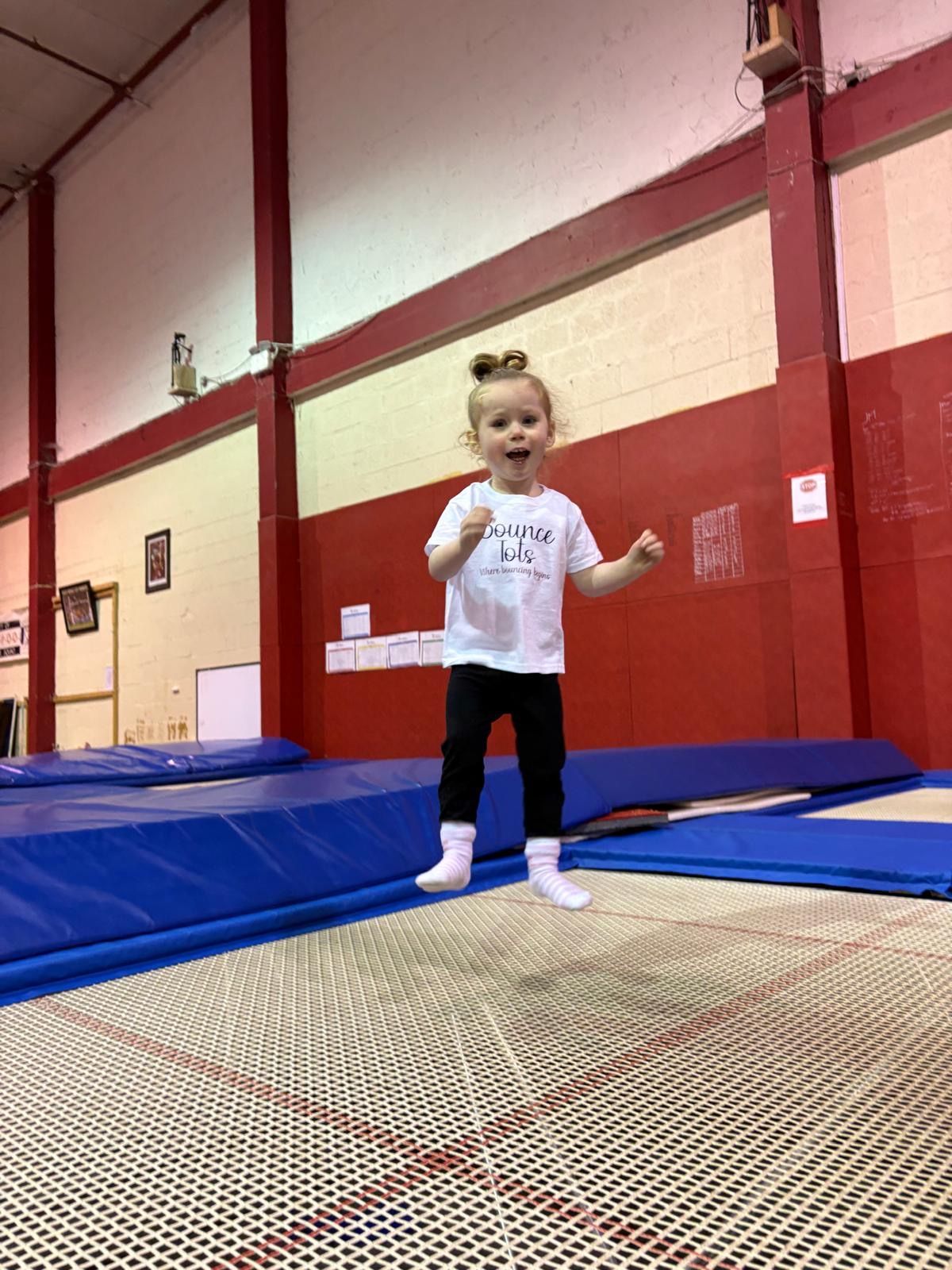 A little girl is jumping on a trampoline in a gym.