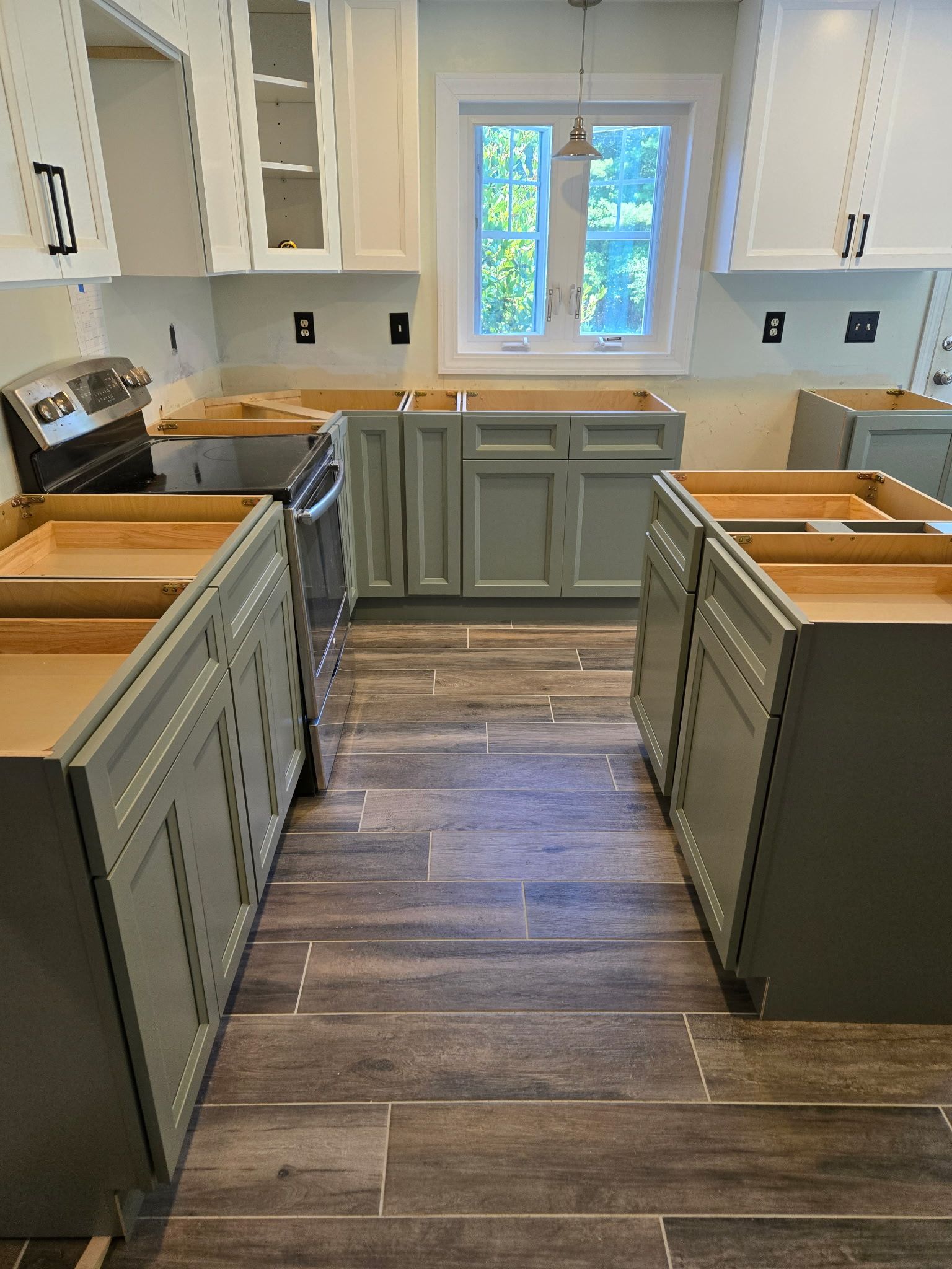 A kitchen under renovation featuring gray lower cabinets, white upper cabinets, and dark wood-look floor tiles.