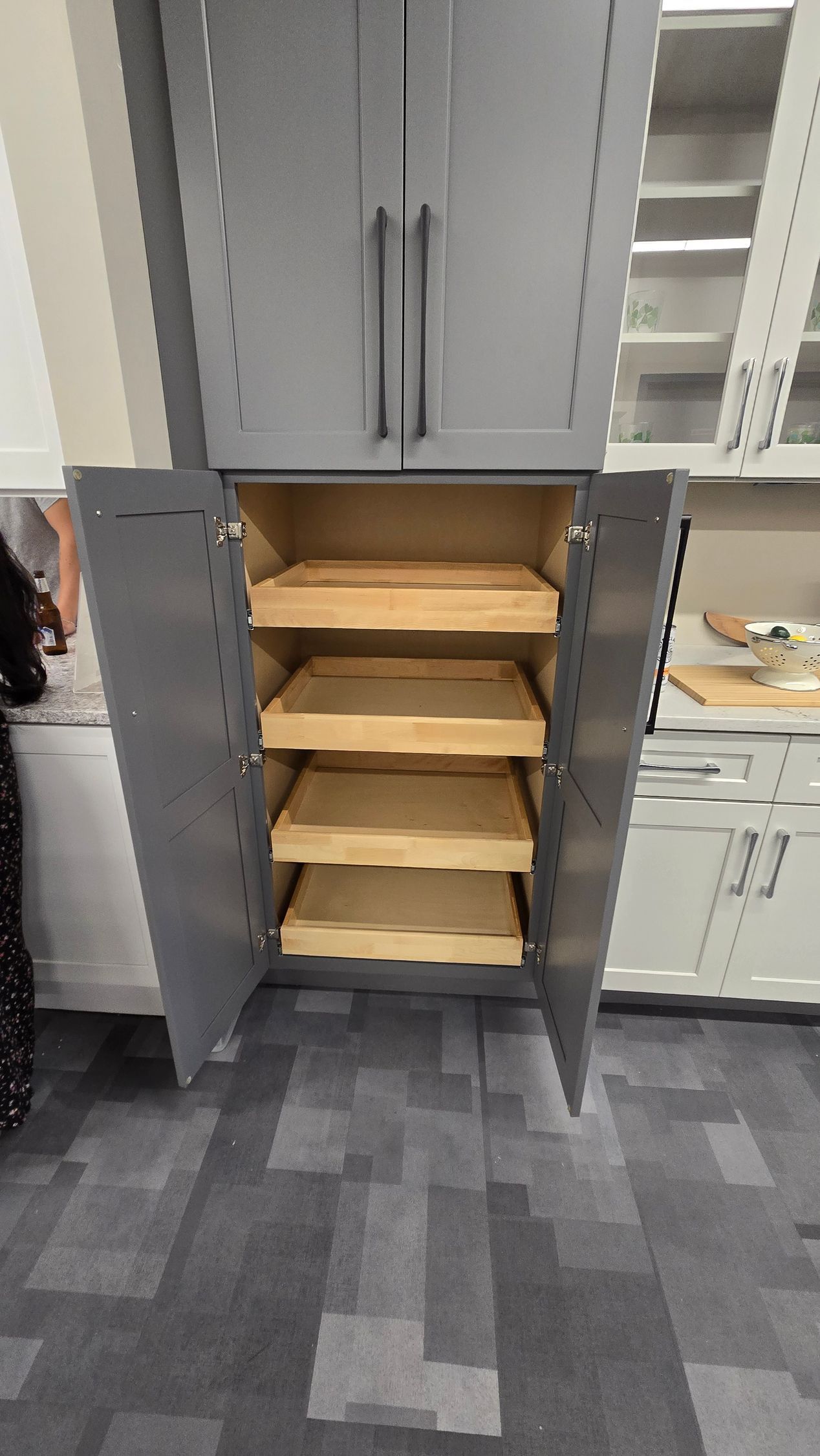 A dark grey kitchen pantry cabinet with double doors open, revealing four natural wood slide-out shelves inside.