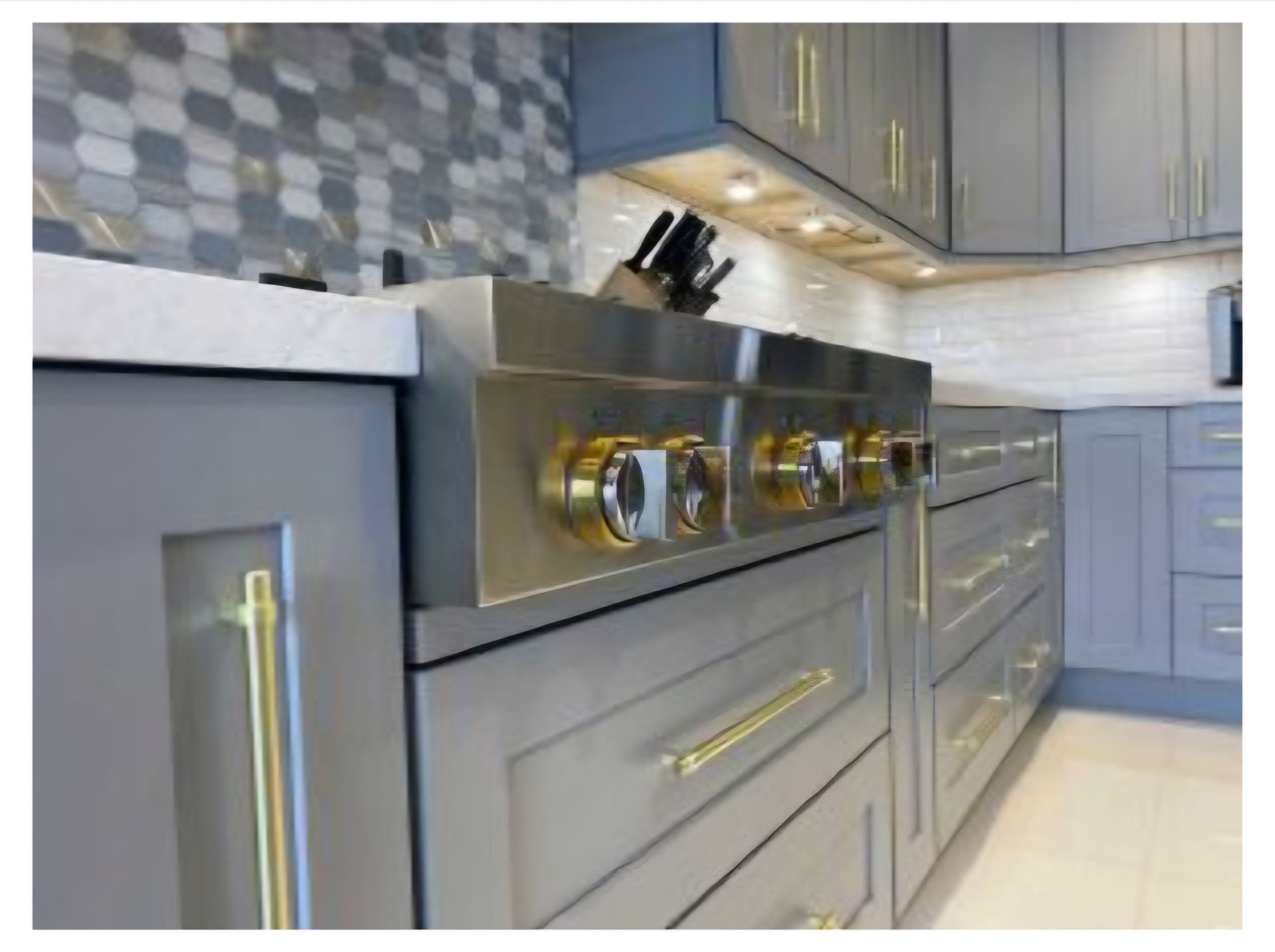 Modern kitchen with gray cabinets, gold hardware, a stainless steel range, and a patterned tile backsplash.