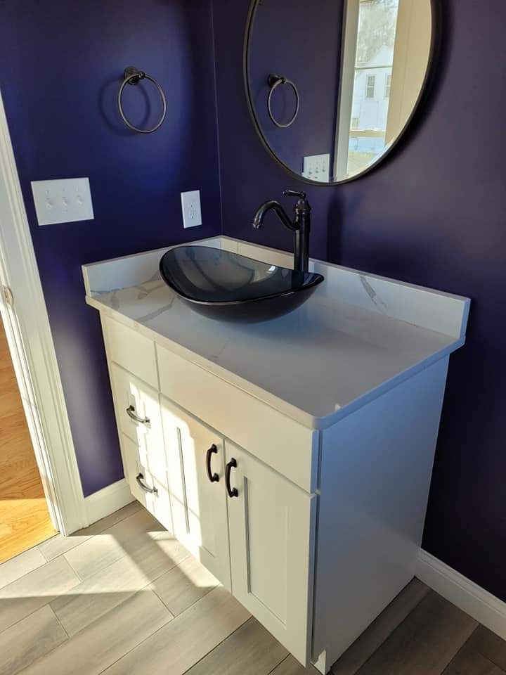 A bathroom vanity with a white cabinet, marble-look countertop, black vessel sink, black faucet, and circular mirror.