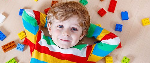 Smiling child lying on the floor with colorful toy blocks around them, wearing a striped shirt