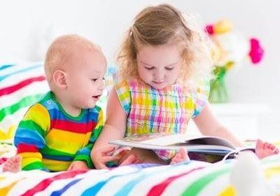 Two children in colorful clothes looking at a book together on a bed