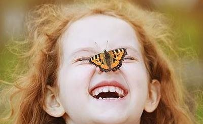 Smiling child with a butterfly resting on her nose outdoors