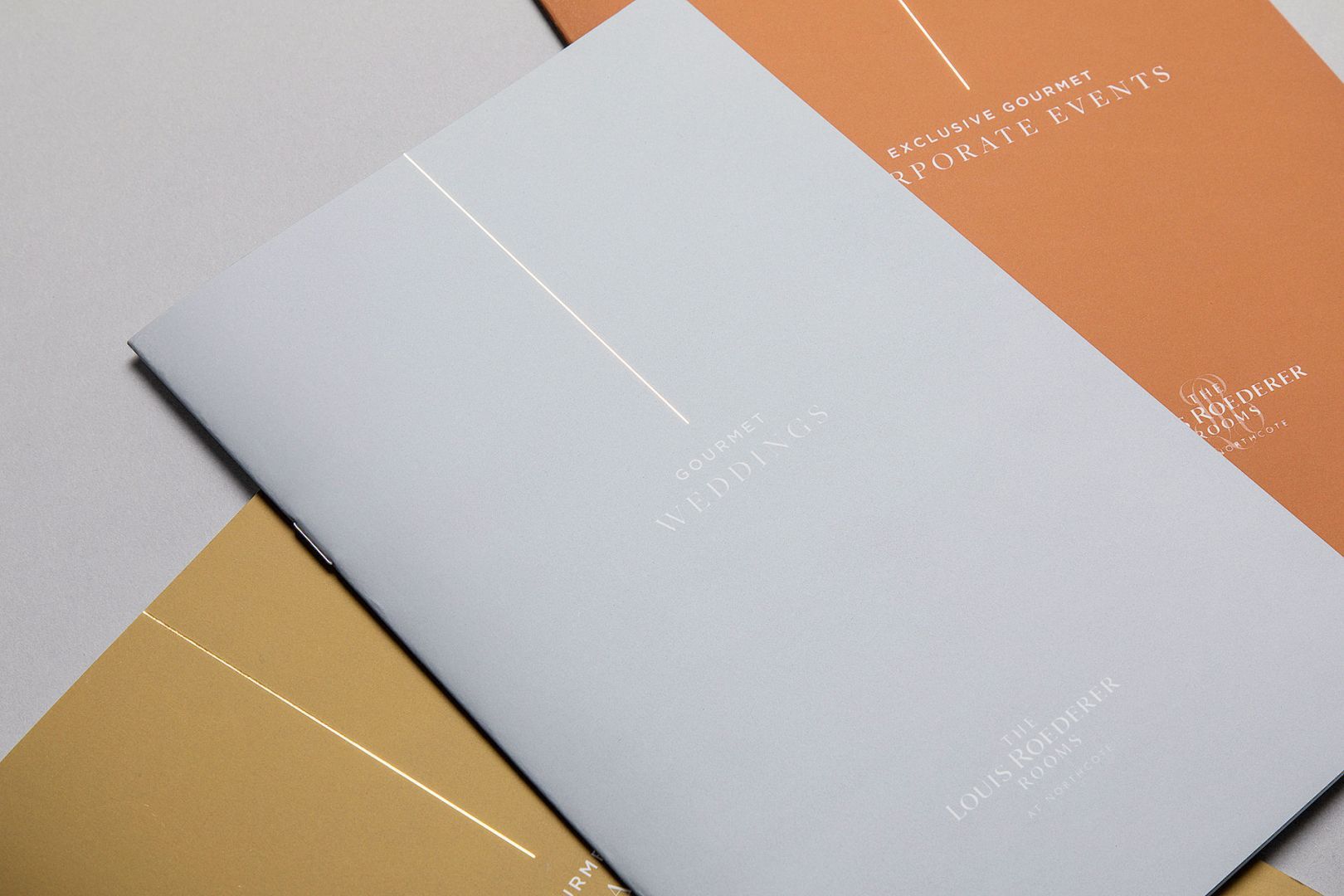 Close-up of three folded brochures, white, tan, and rust colored, stacked on top of each other.