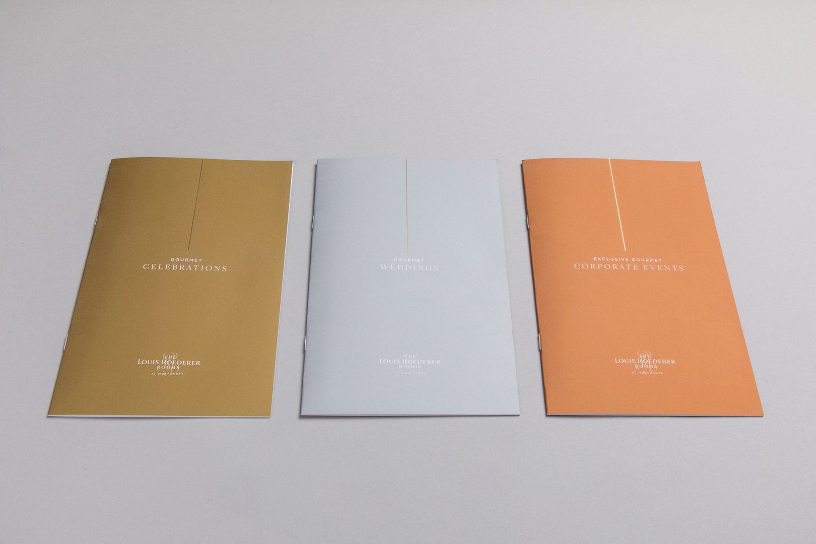 Three brochures: gold, white, and orange, each with a centered vertical line of dots and text.