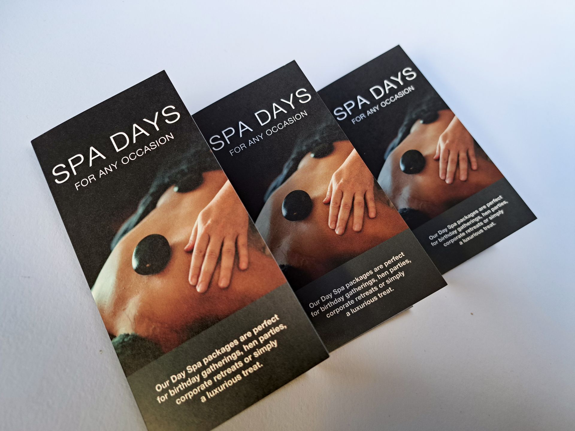 Three brochures advertising spa days. The brochures display a person's back with stones and hands.