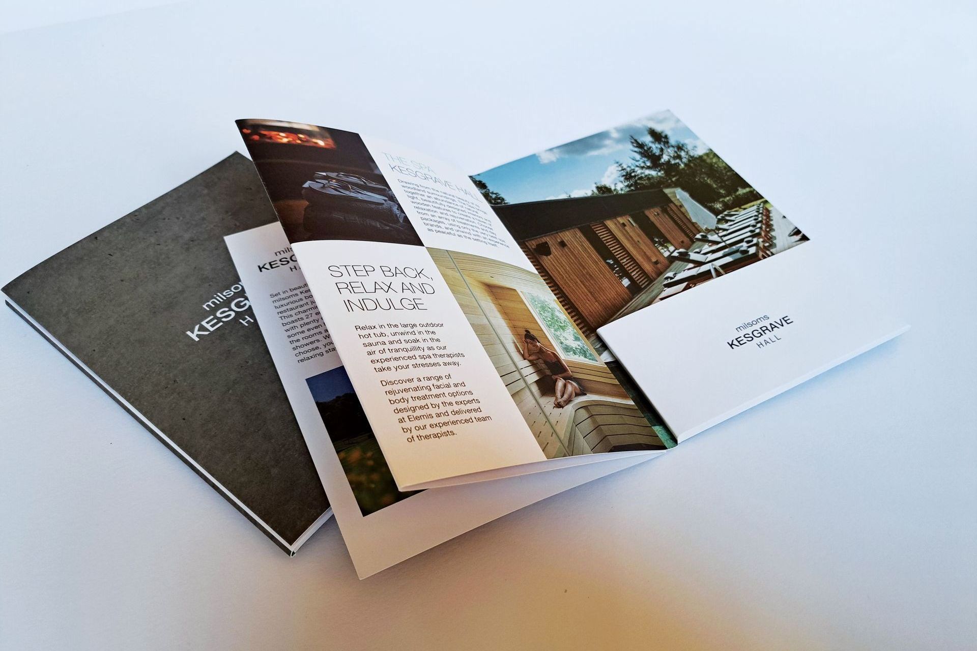 Brochure, partially open, with photos and text, on a white surface. Gray cover, white interior pages.