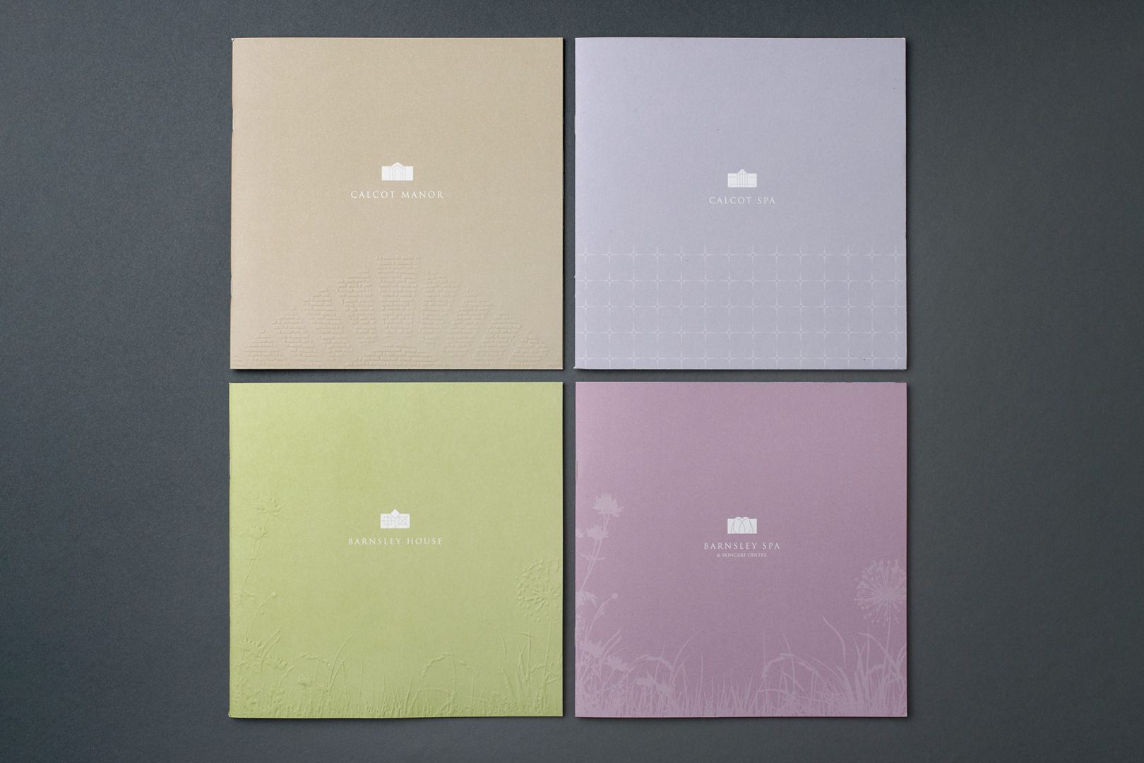 Four square brochures in tan, light purple, green, and pink, each with a small cloud icon and text, on a gray surface.