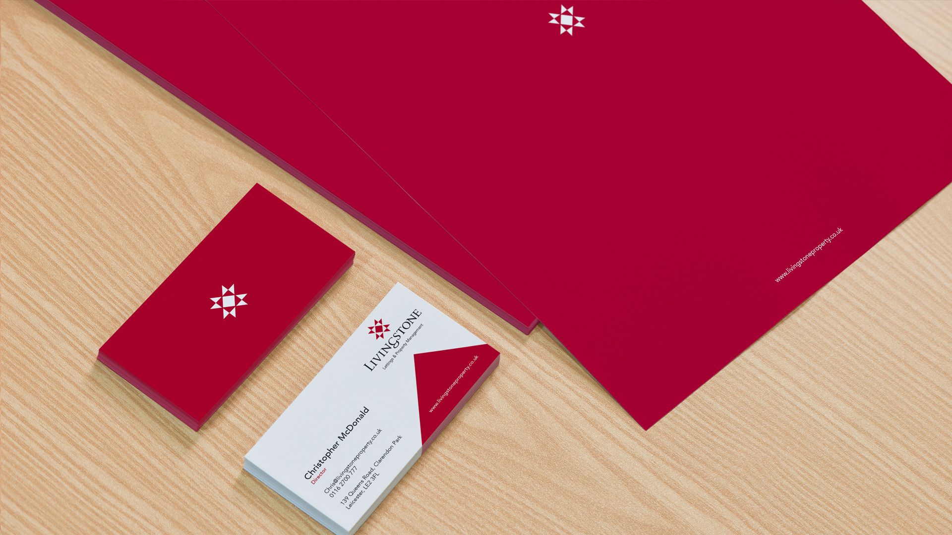 Red stationary and business cards with white logo on a wood grain surface.