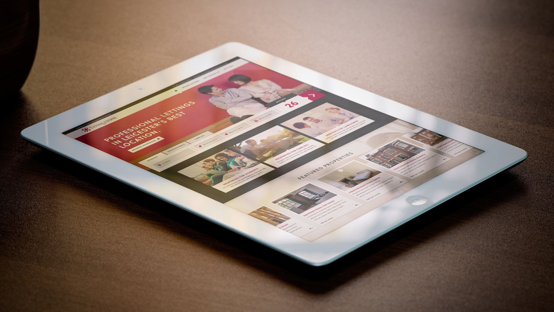 Tablet on a brown surface displaying a website with red and white elements and various images.