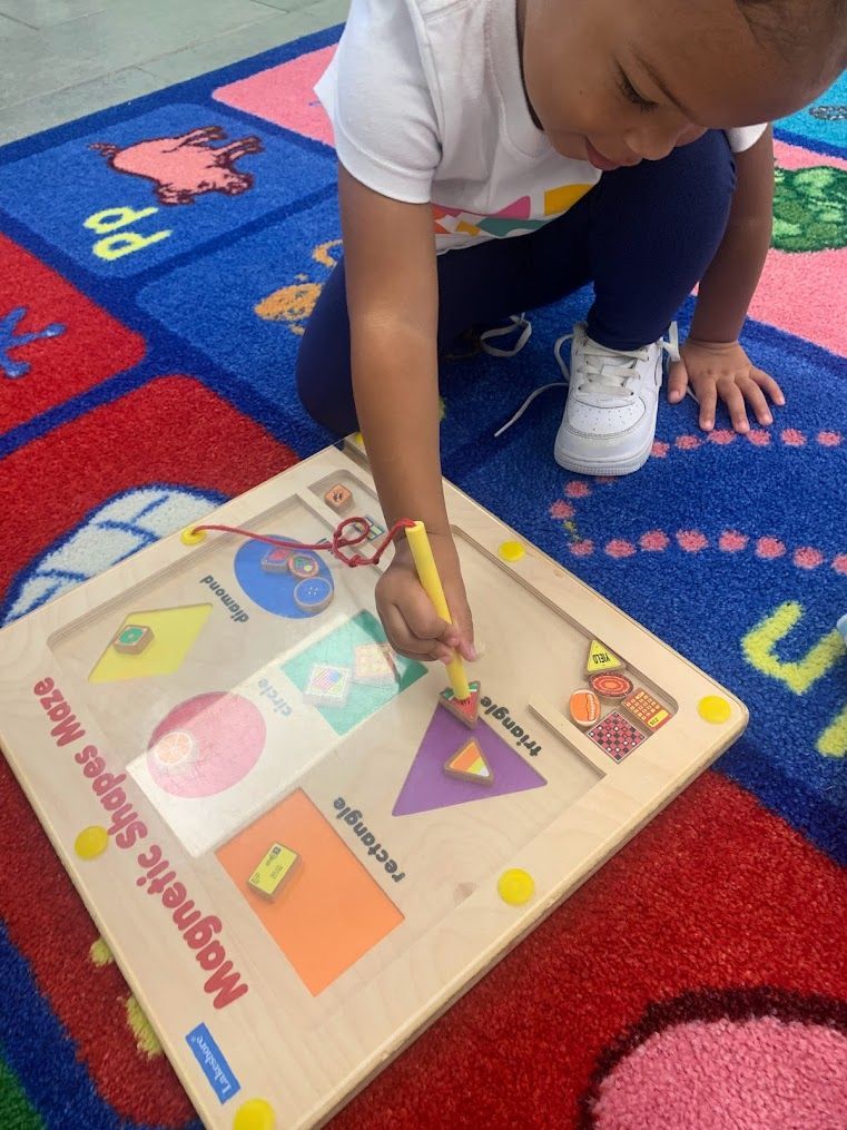 A child is playing with a magnetic shapes maze on the floor.