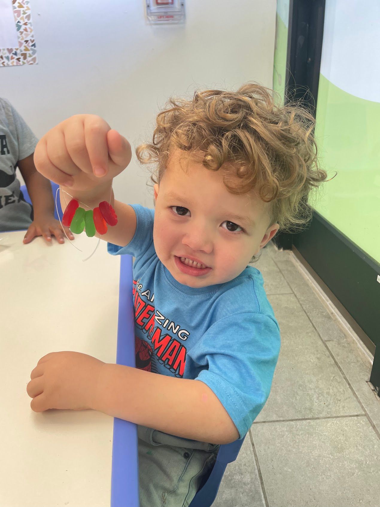 A young boy is sitting at a table holding a gummy bear
