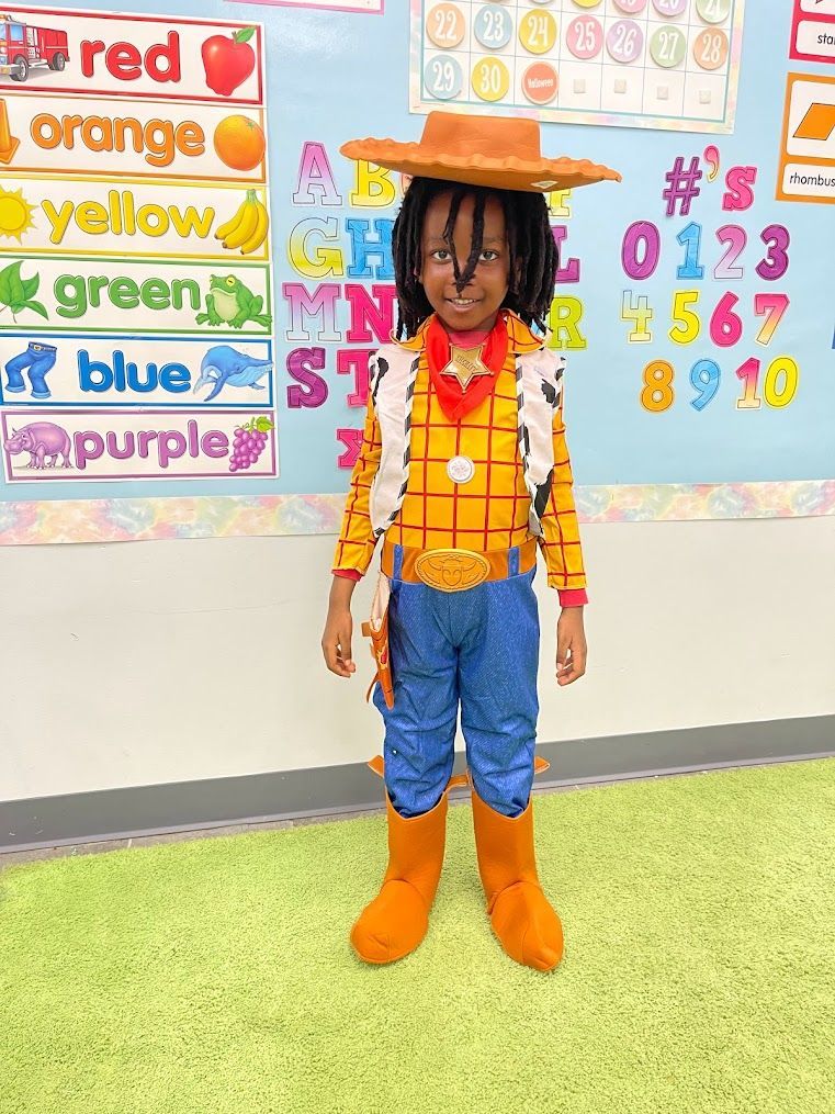 A young boy in a woody costume is standing in a classroom.