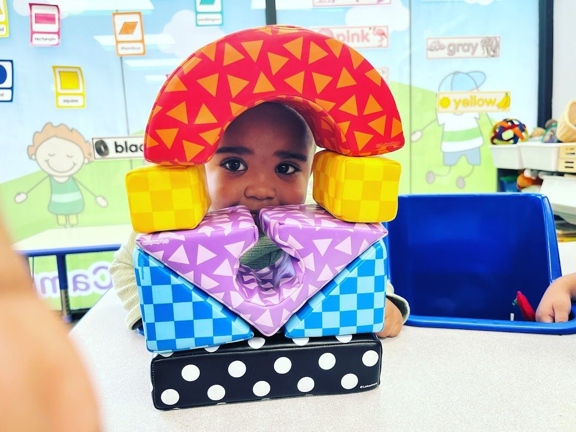 A child is sitting at a table with a colorful toy in front of his face.