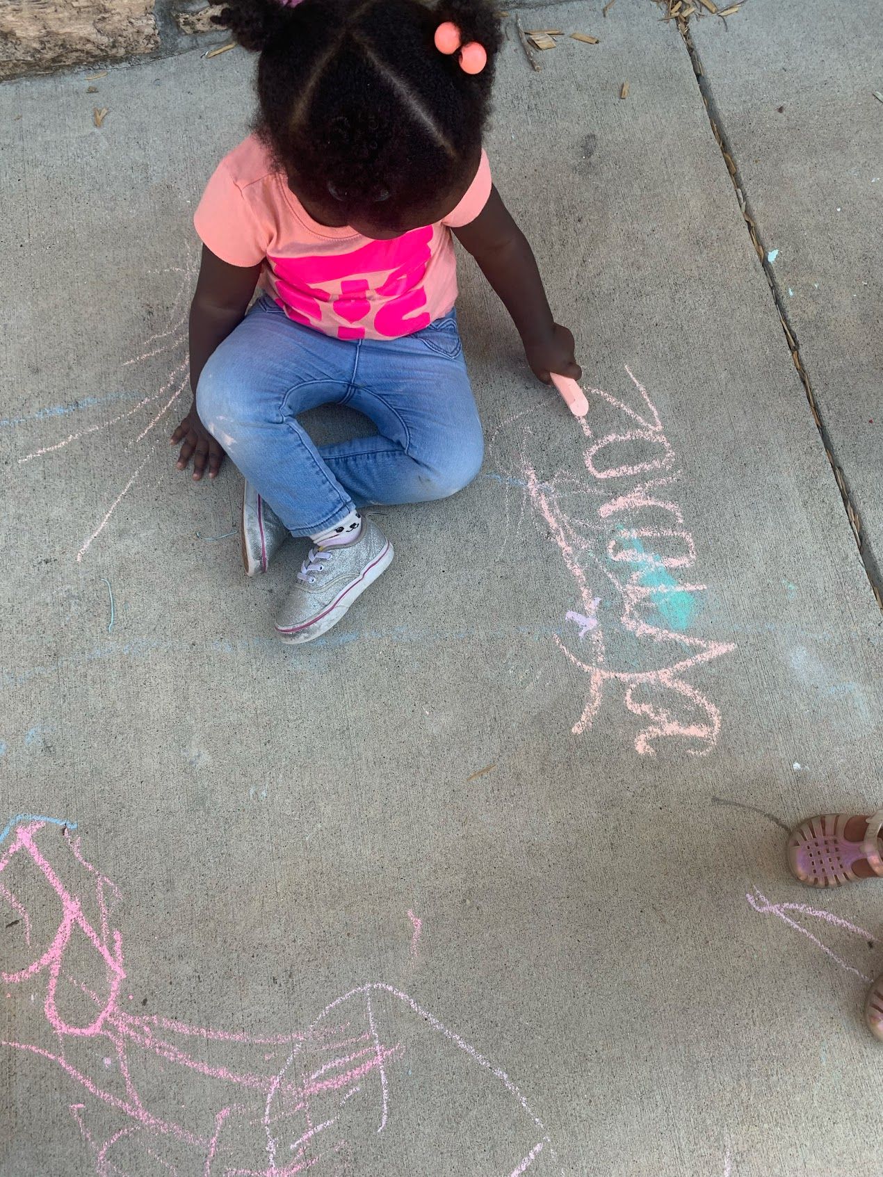 A little girl is kneeling down on the sidewalk drawing with chalk.
