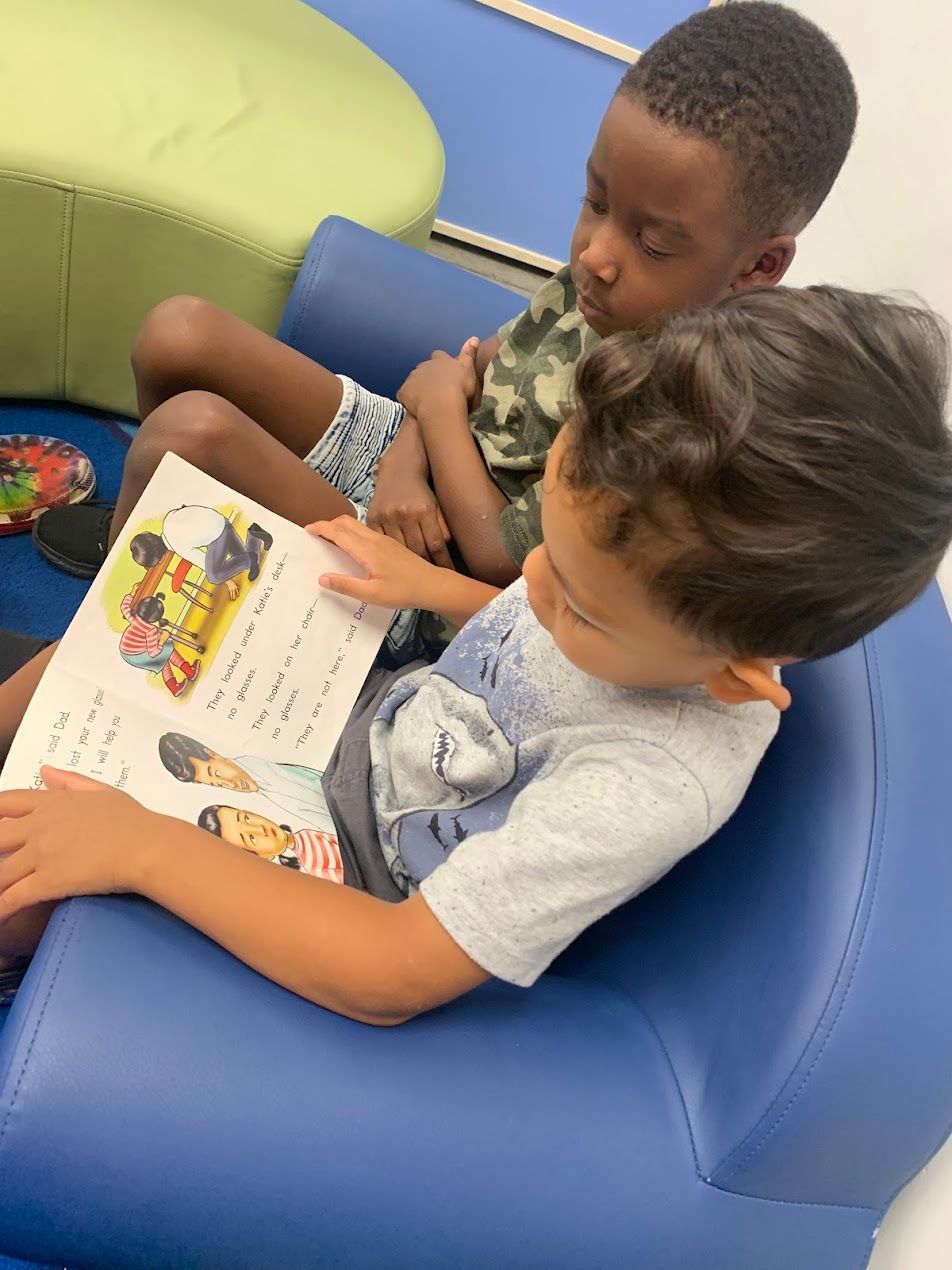 Two young boys are sitting on a blue chair reading a book together.