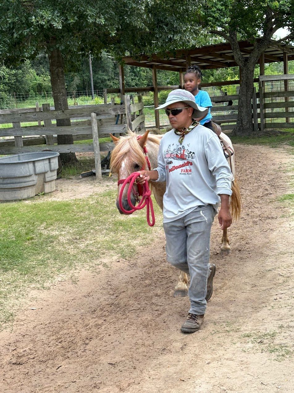 A man is leading a child on a pony in a dirt field.