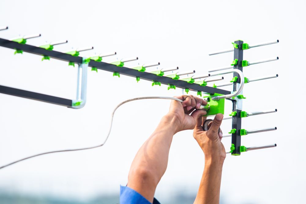 Technician connecting coaxial cable to TV antenna during installation on rooftop for signal setup
