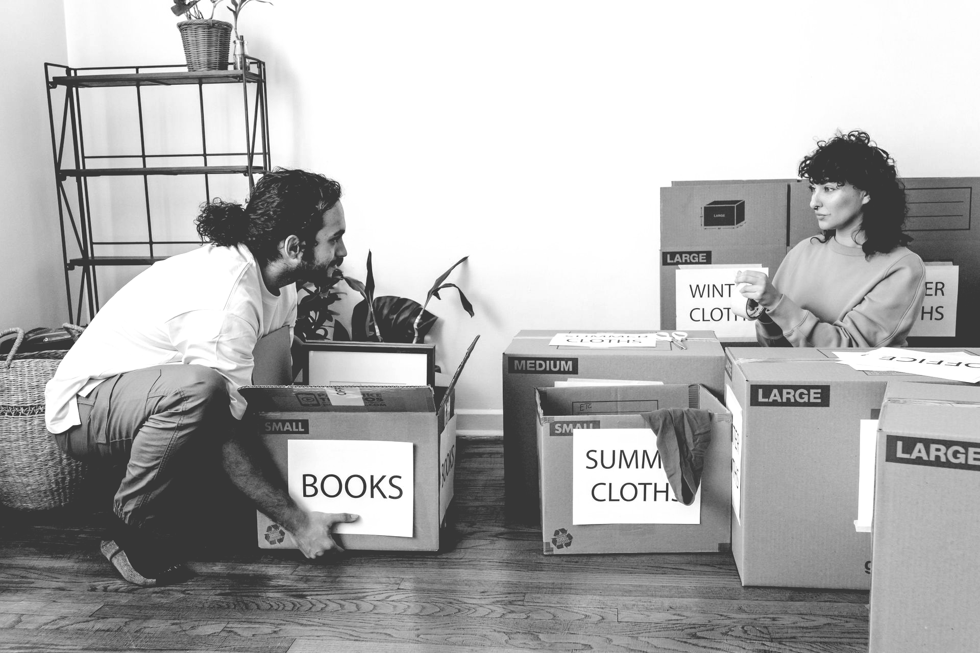 A couple sits on the floor packing cardboard boxes labeled