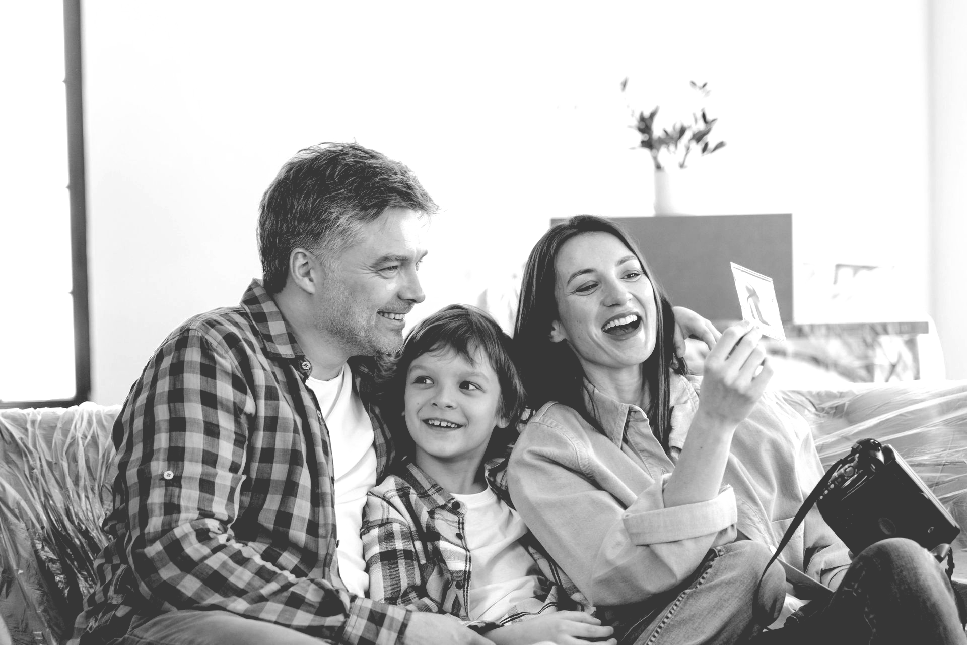 A family sitting together on a sofa, smiling while looking at a small photo held by a woman.