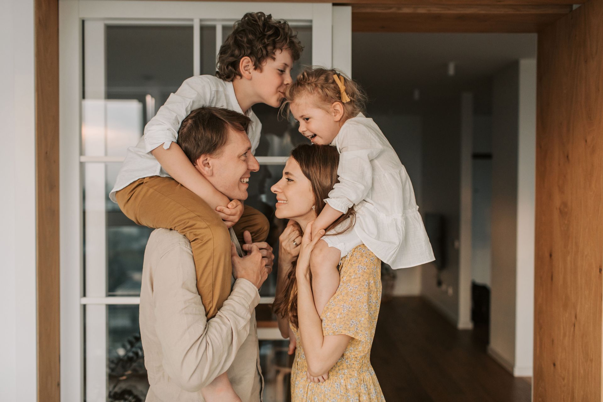 Family group hug in a doorway, with two adults and two children smiling indoors.