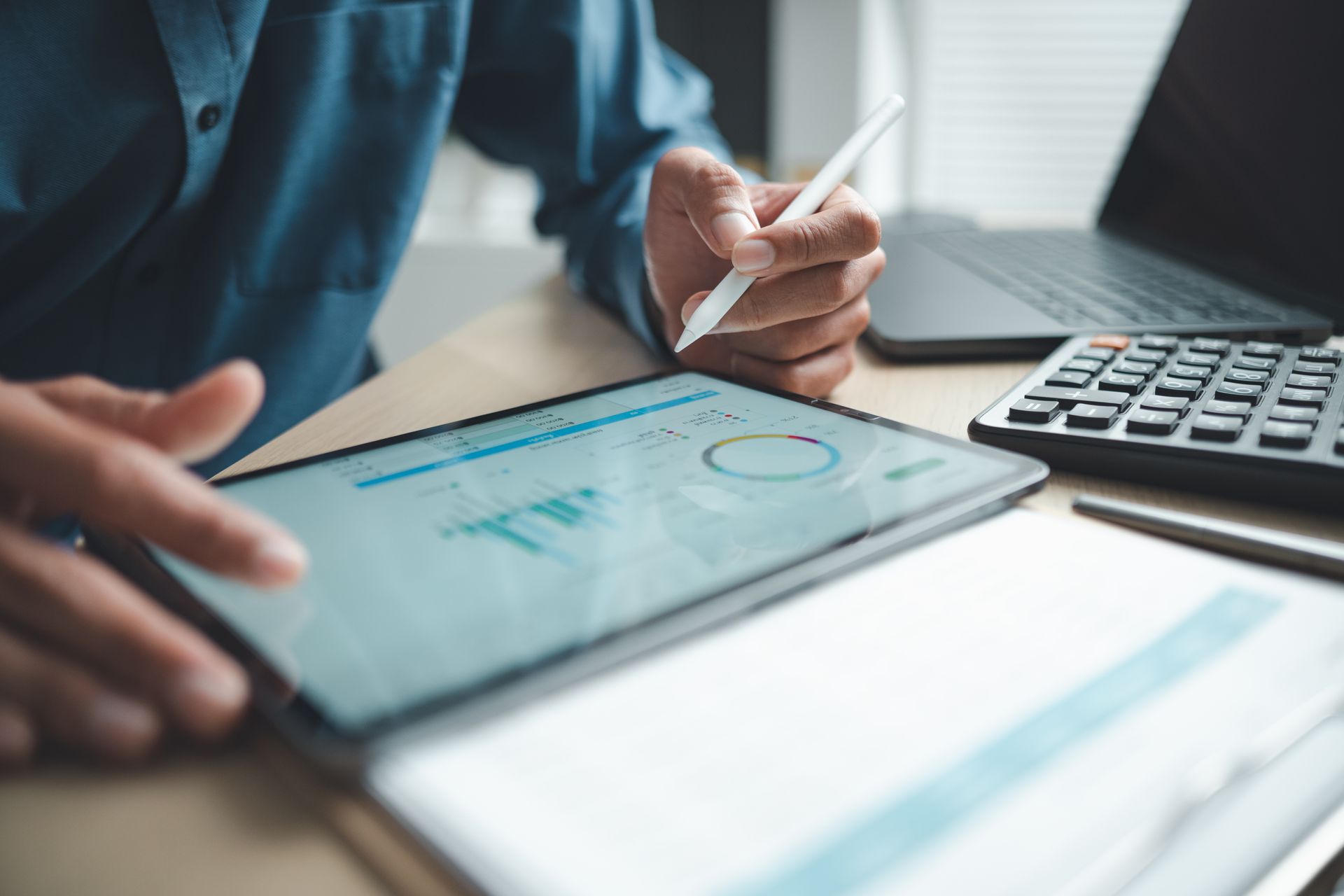 Person reviewing financial charts on a tablet beside a calculator and notebook on a desk