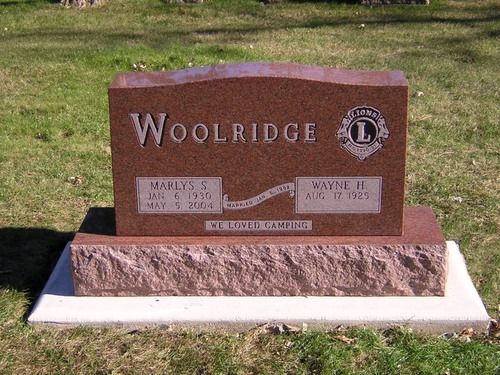 A red granite Woolridge family headstone with engraved names and dates, set in a grassy cemetery.