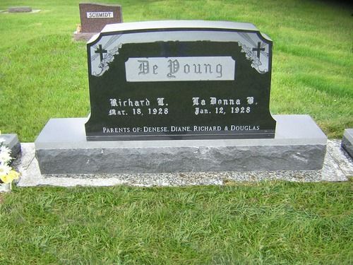 A black granite double headstone for the De Young family with names and dates, situated in a grassy cemetery.