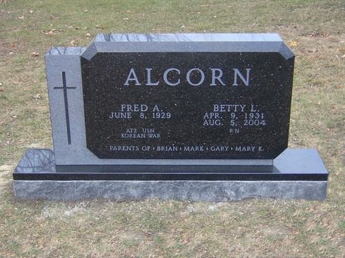 A black granite double gravestone for the Alcorn family, featuring a cross, names, dates, and names of their children.