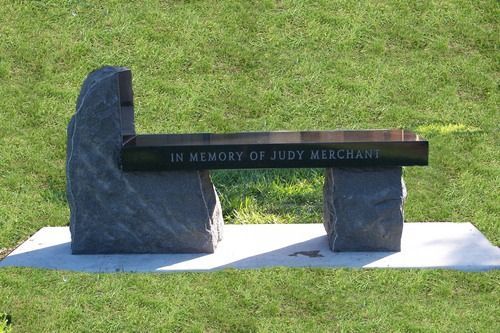 A stone memorial bench with a black seat inscribed 