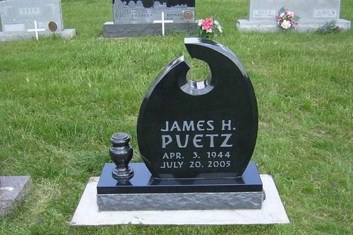 A black granite tombstone in a grassy cemetery, inscribed with 